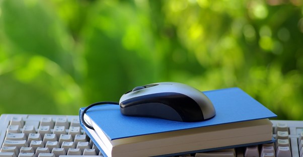 a book and computer mouse on a keyboard symbolizing online colleges